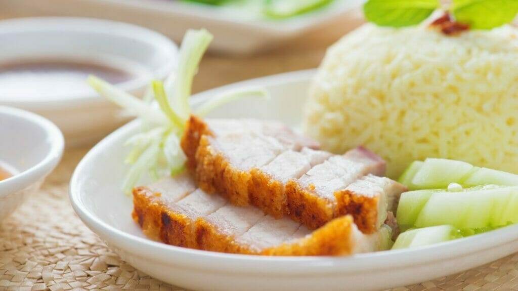 Ein weißer Teller mit Schweinefleisch, Reis und Gemüse.